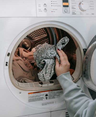 A person pulling freshly dried laundry from a dryer, holding a patterned garment with a cozy, clean look.