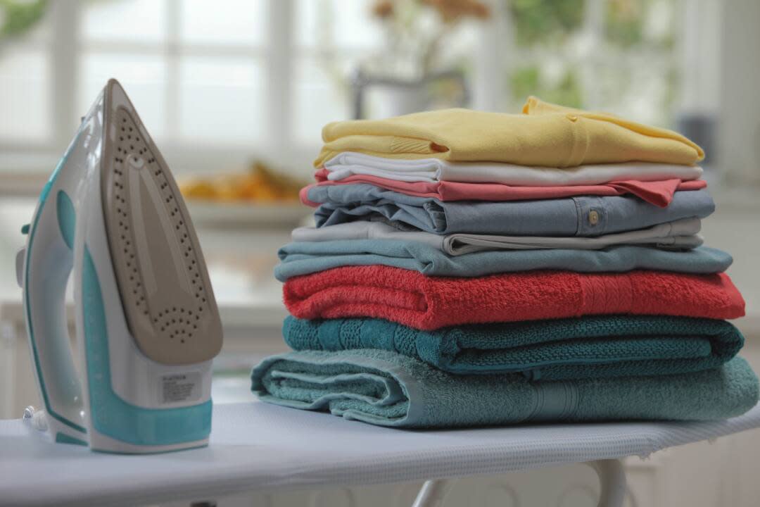a steam iron next to a neatly stacked pile of ironed clothes and towels on an ironing board