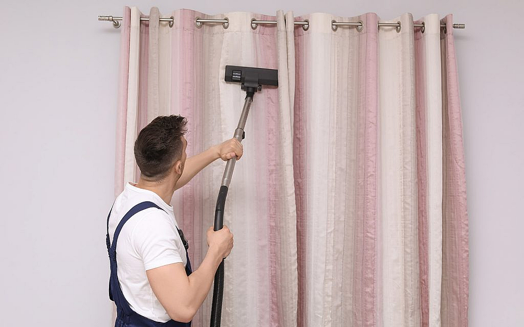 A man cleaning curtains using a vacuum cleaner